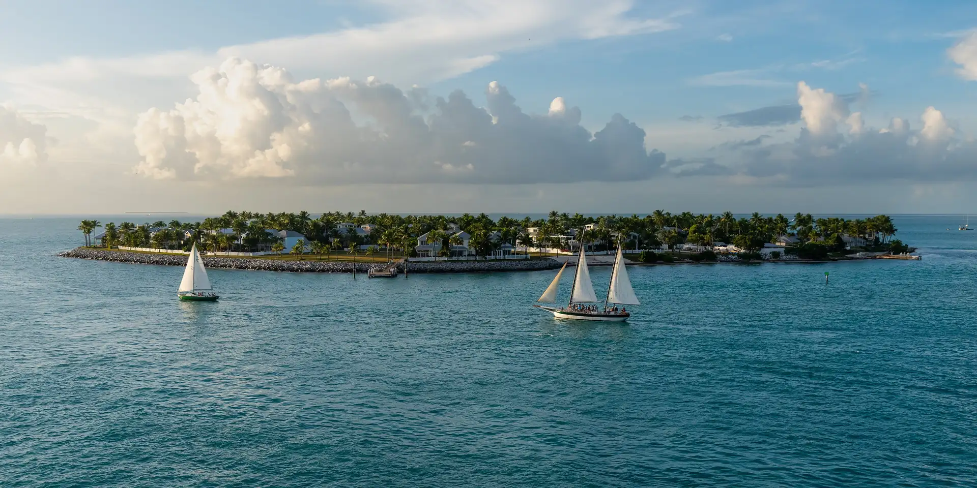 Sailboats passing Sunset Key, a small palm-covered island in the Florida Keys, under late afternoon clouds